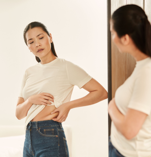 woman in front of a mirror pinching her belly skin